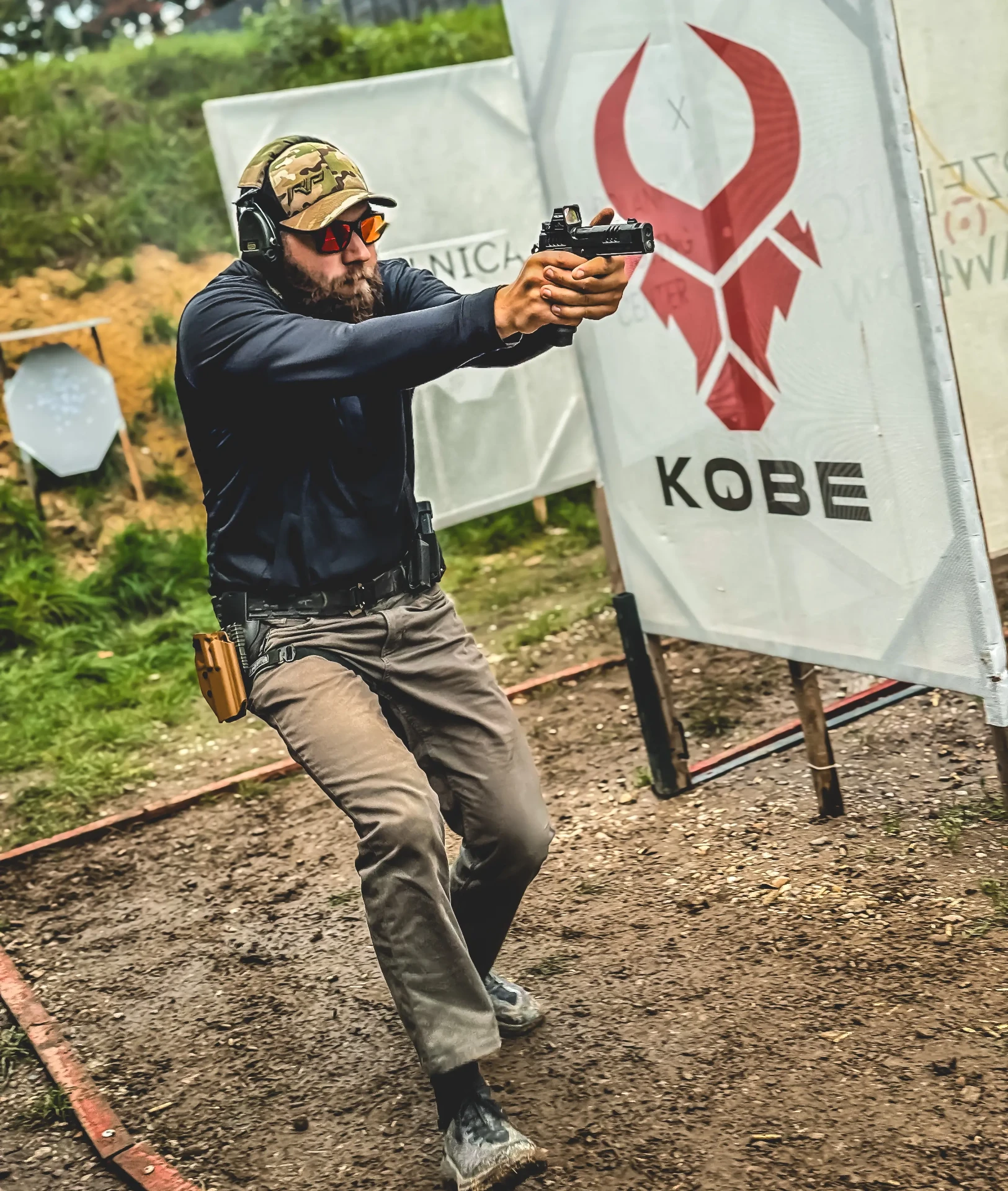 Tireur accroupi visant avec un pistolet Glock doté d’une optique à point rouge sur un stand de tir en Pologne