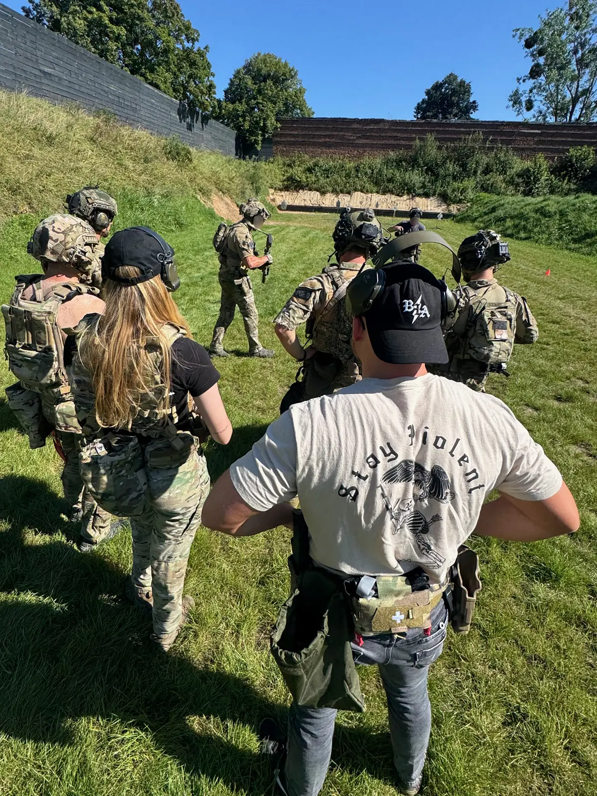 Group of international shooters in tactical gear during a live-fire training briefing at a Polish outdoor range